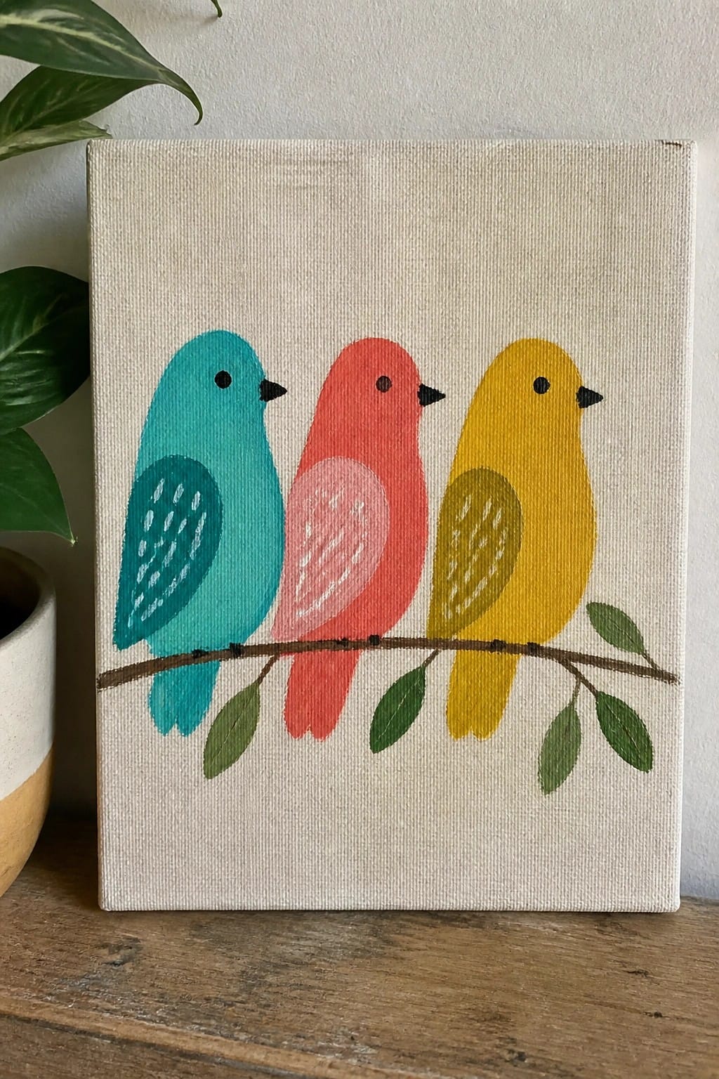 Three stylized birds in turquoise, coral, and yellow perched on a leafy branch