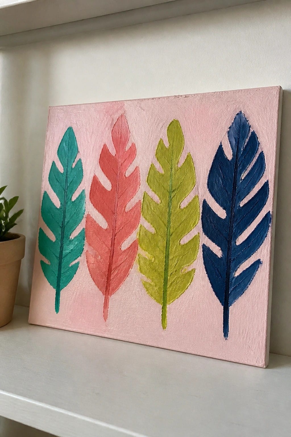 Four colorful painted leaves on pink canvas atop white shelf