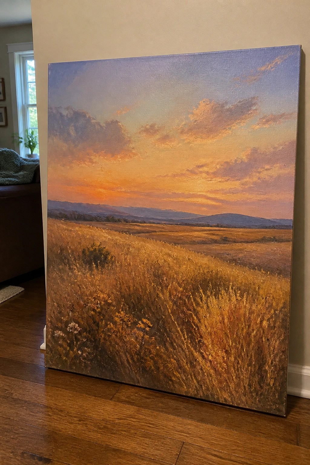 Golden field at sunset with orange-purple sky, large canvas leaning on wooden floor.