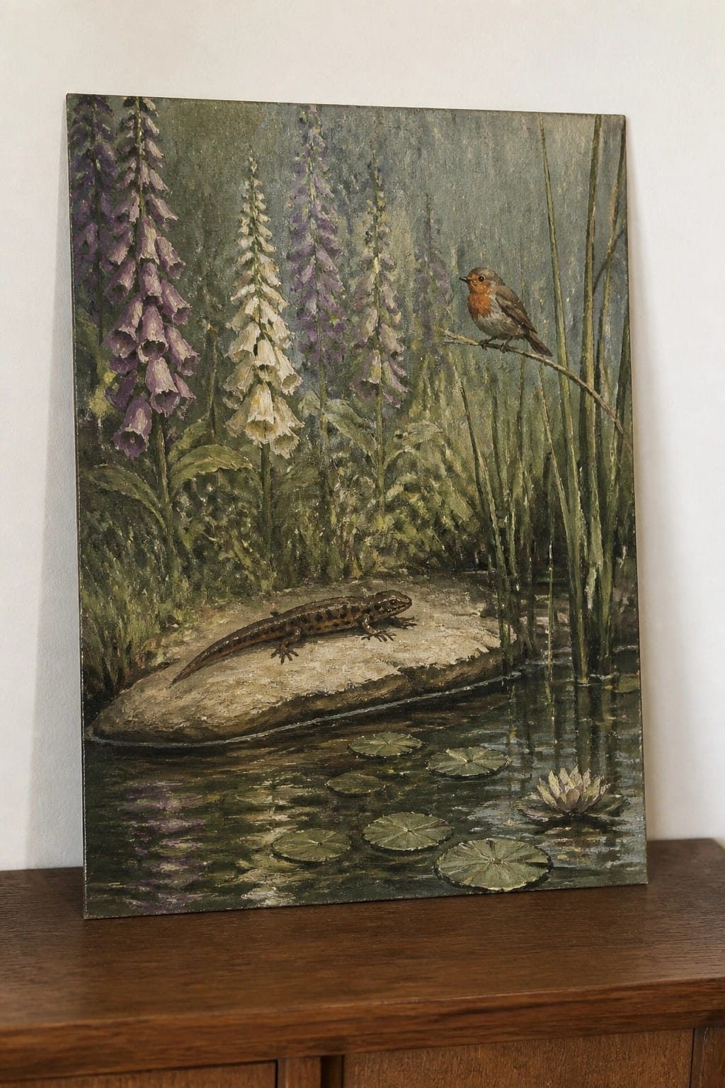 Painting of foxgloves, robin on branch, and salamander on rock in lily pond.