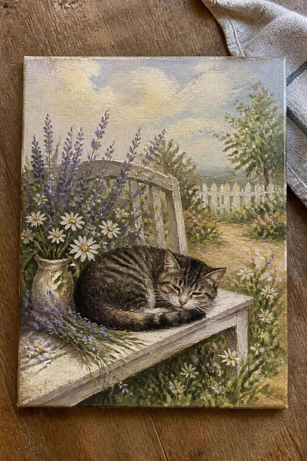 Sleeping tabby cat curled on wooden bench amid lavender and daisies in garden