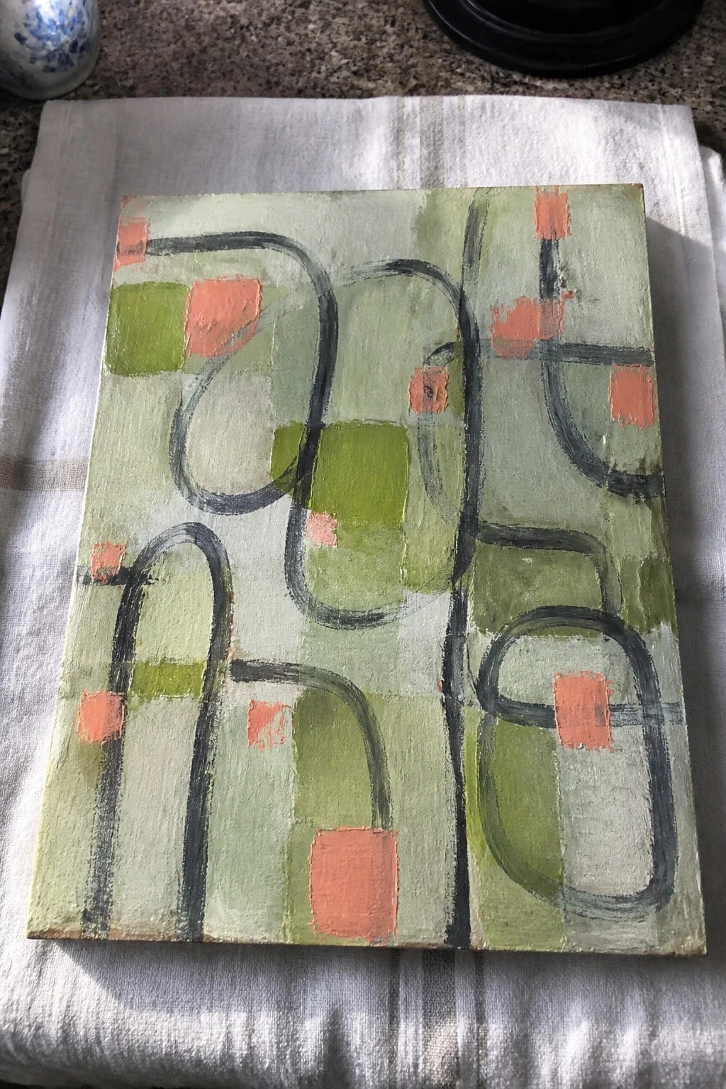 Abstract painting with green washes, black curves, and orange squares on white cloth.