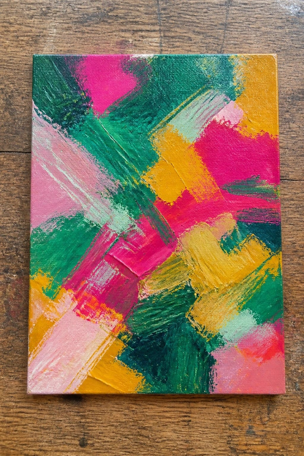 Vibrant abstract painting with bold pink, green, yellow, and orange brushstrokes on wood.