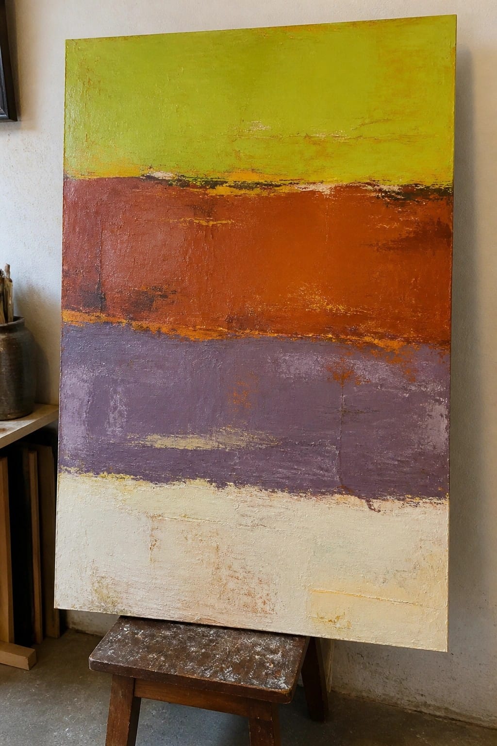 Abstract painting with horizontal green, orange, purple, and beige stripes on wooden stool