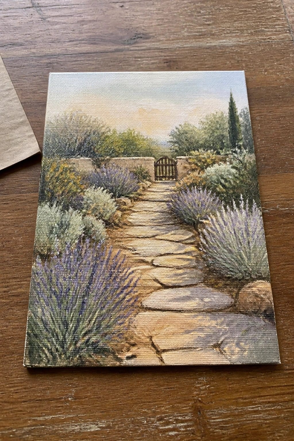 Stone path lined with lavender leading to wooden gate amid green shrubs and trees.