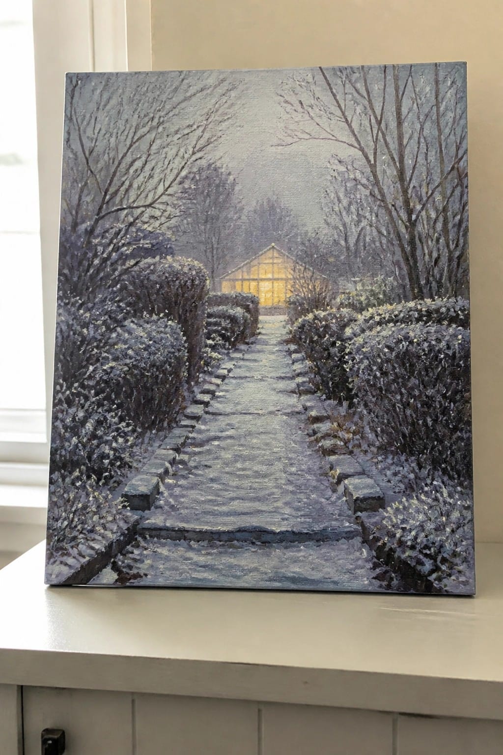 An oil painting of a snowy path lined with snow-covered bushes leading toward a lit greenhouse between bare trees.