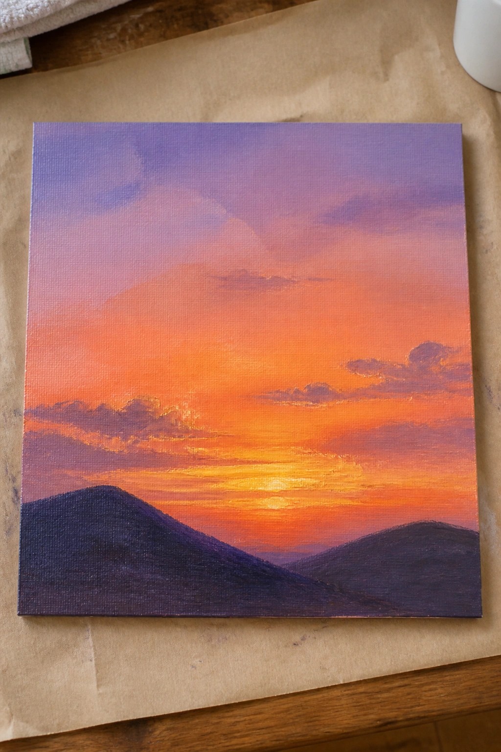 Vibrant sunset painting with orange-purple skies over dark silhouetted hills on canvas