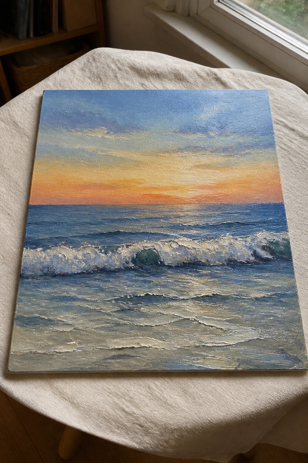 Painting of crashing ocean waves at sunset on white cloth-covered surface