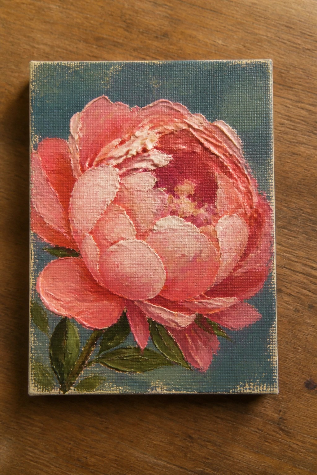 Textured pink peony painting on canvas with teal background and green leaves