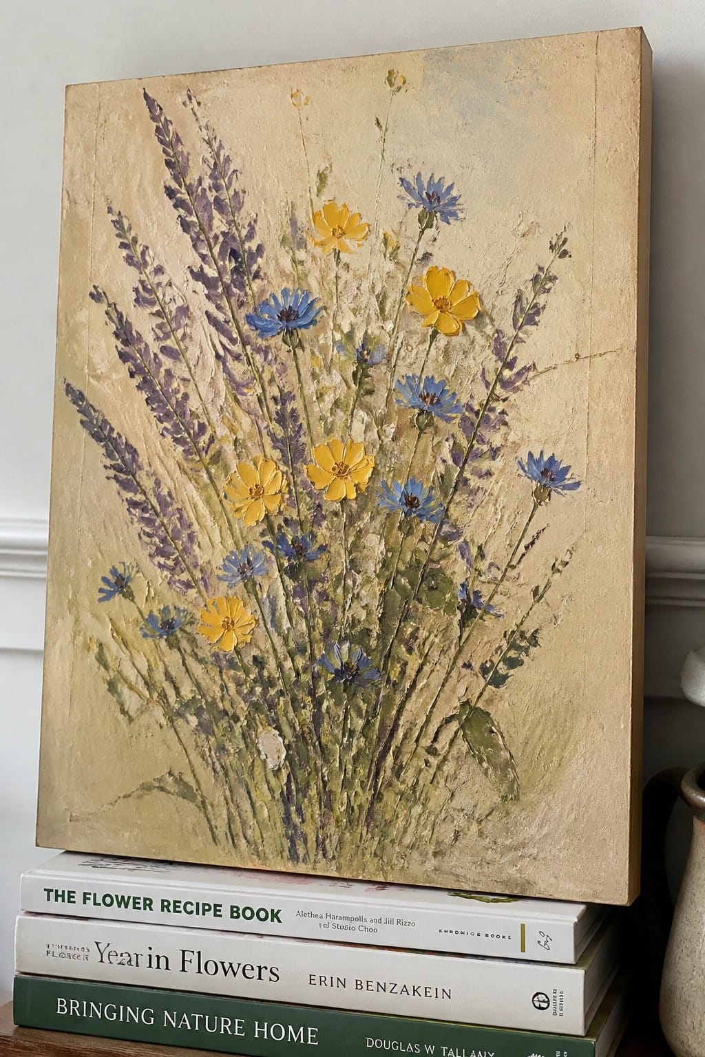Painting of yellow and blue wildflowers atop stacked flower books