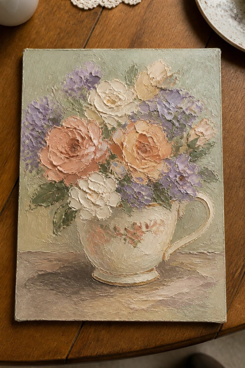 Impasto oil painting of roses and hydrangeas in a white pitcher on wood.