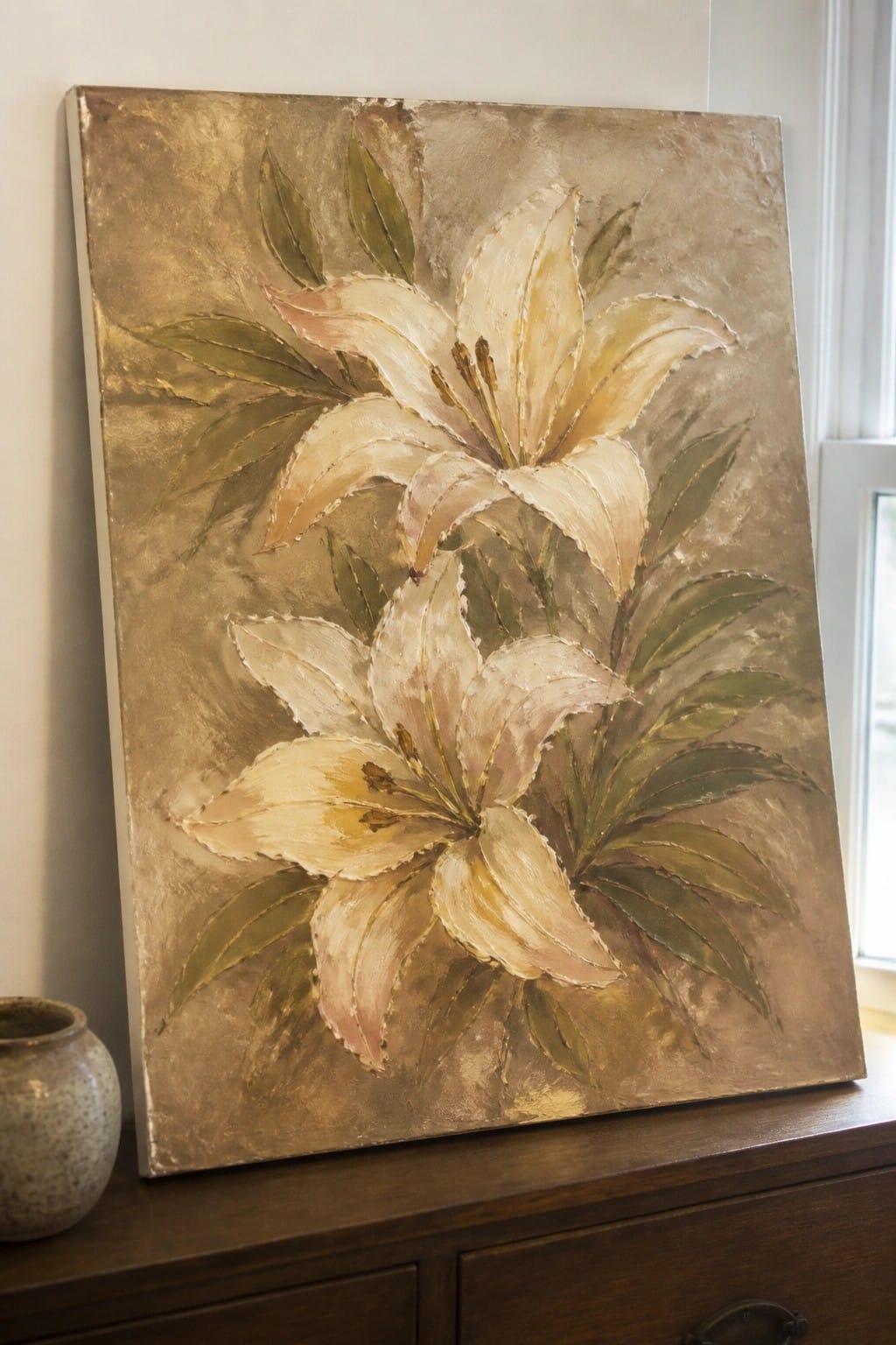 Textured painting of white lilies with green leaves on gold background atop wooden dresser