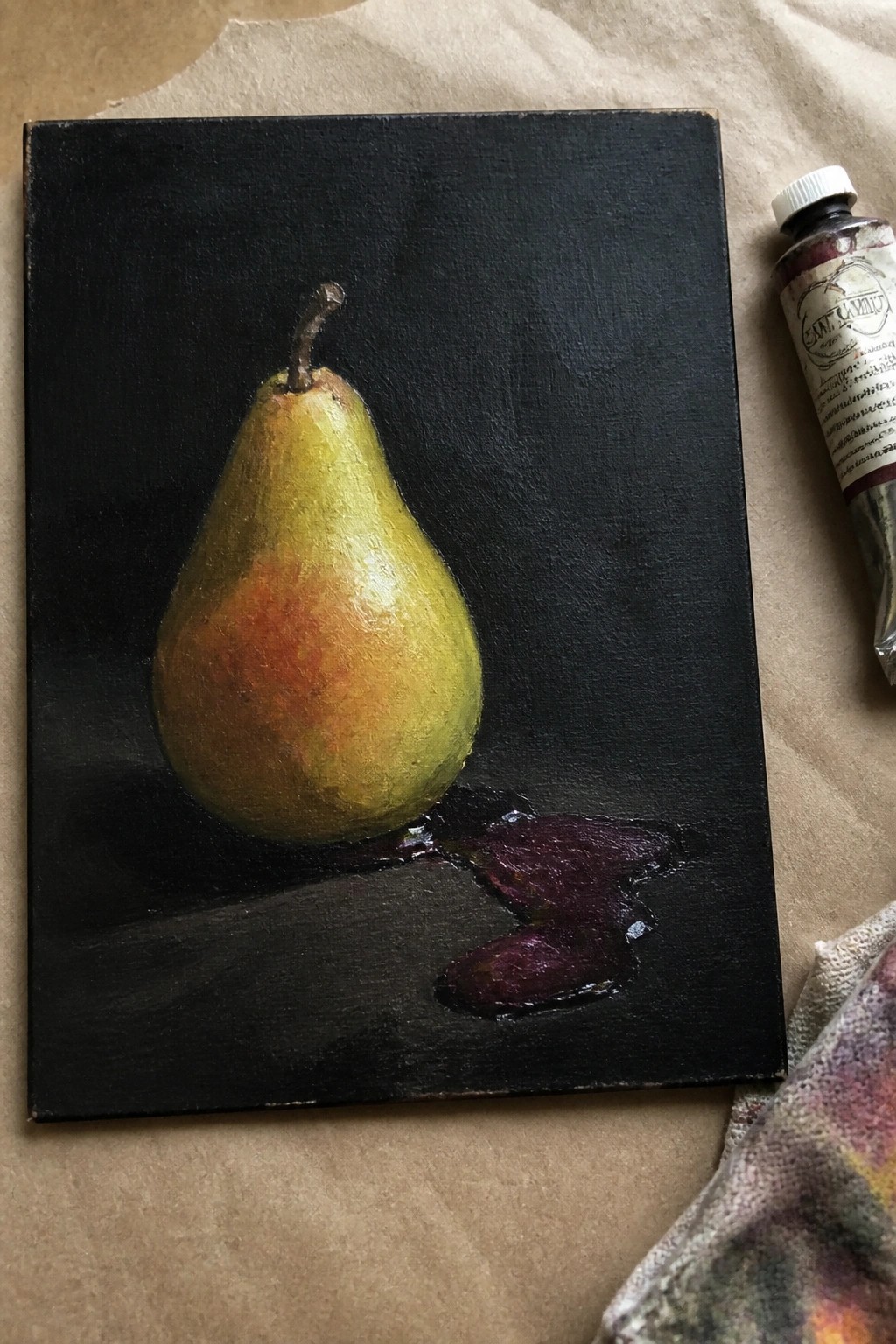 A realistic oil painting of a single pear on a black canvas with a purple spill at its base and a tube of paint nearby.