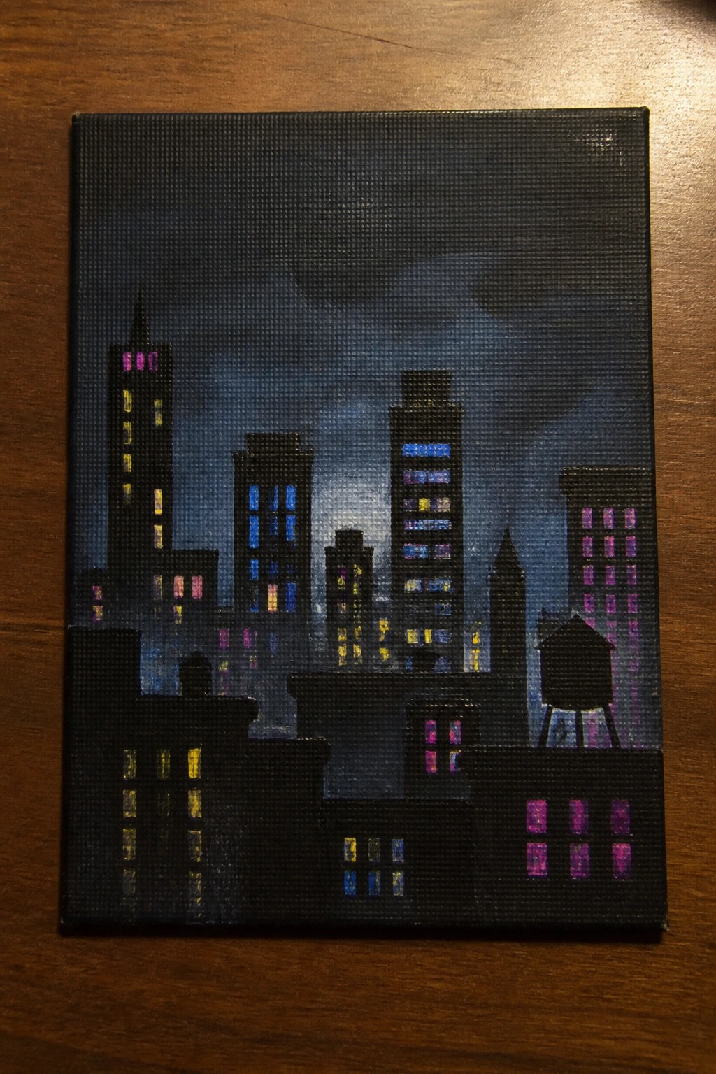 Night cityscape painting on canvas showing skyscrapers with colorful glowing windows and water tower.