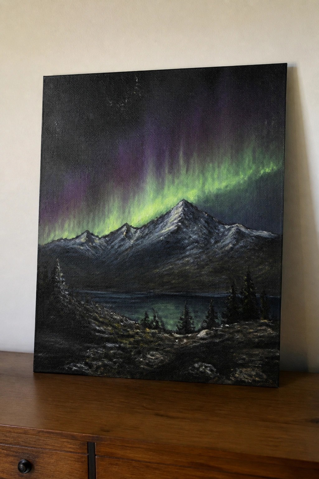 Vibrant green and purple aurora over snow-capped mountains and a dark lake at night