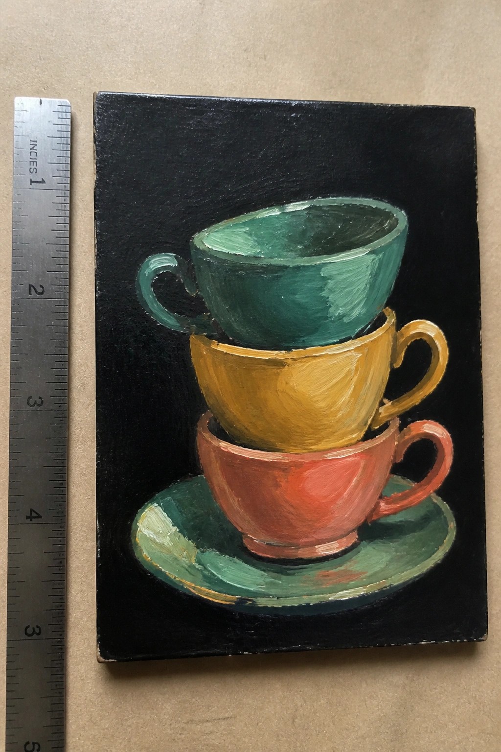 Stacked green, yellow, and red teacups painting beside metal ruler on beige surface