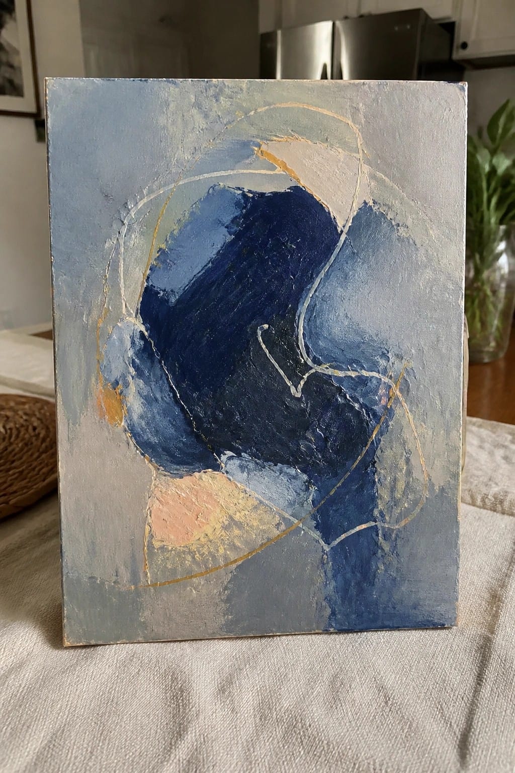 Abstract painting with bold blue shapes, gold lines, peach accents, and textured grays on canvas