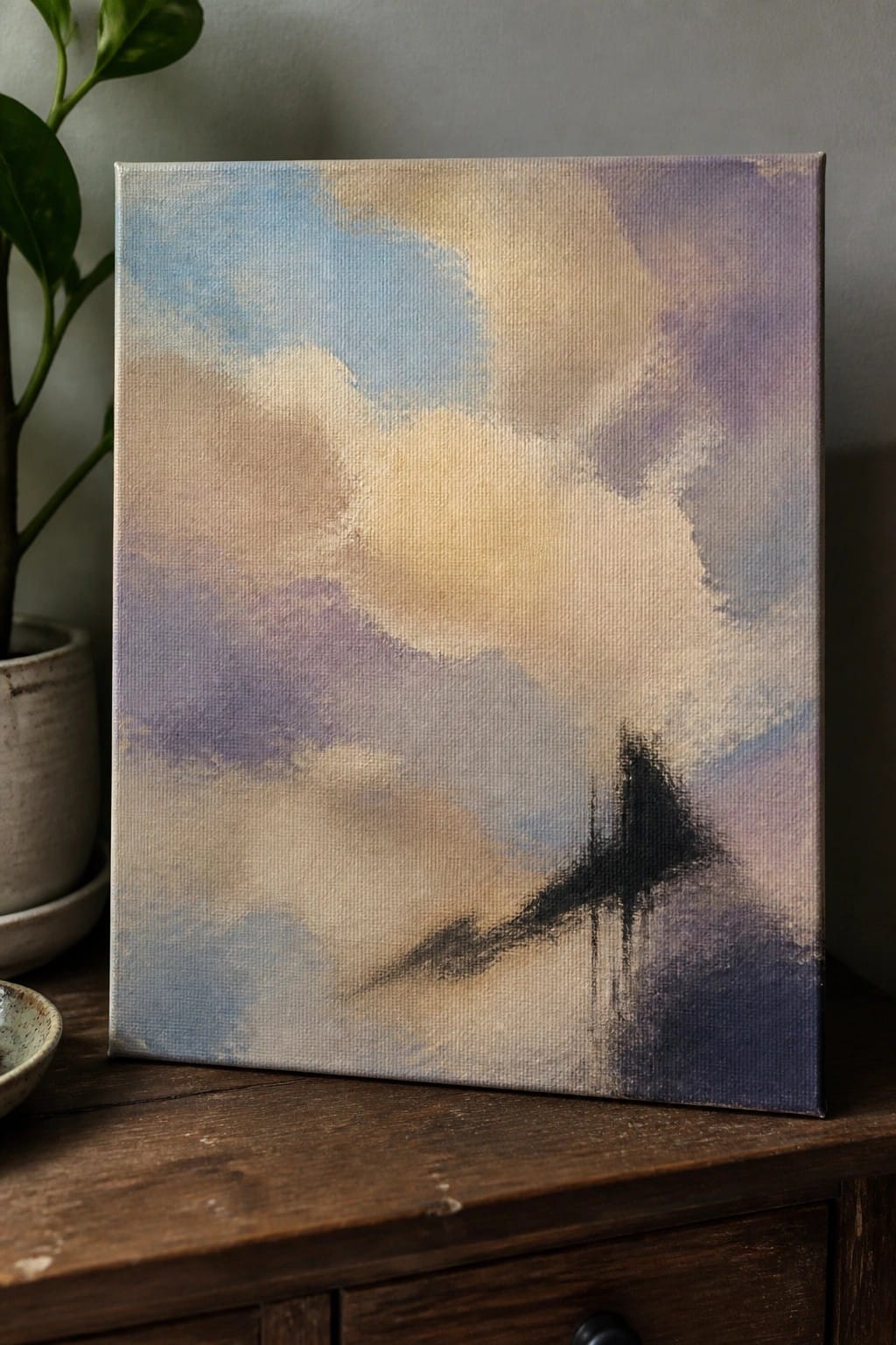 Abstract painting in soft blues purples and beiges beside potted plant on wood