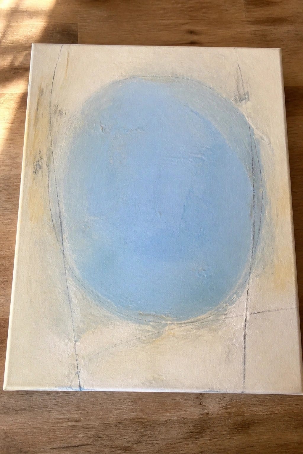 Abstract painting with large light-blue oval on textured off-white canvas over wood floor.