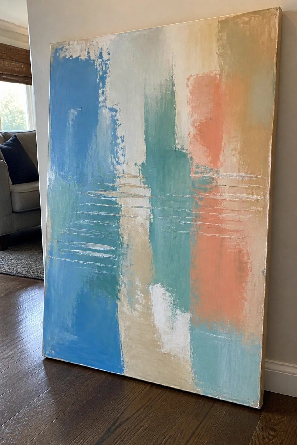 Large abstract painting with blue, teal, orange, beige brushstrokes leaning on wooden floor