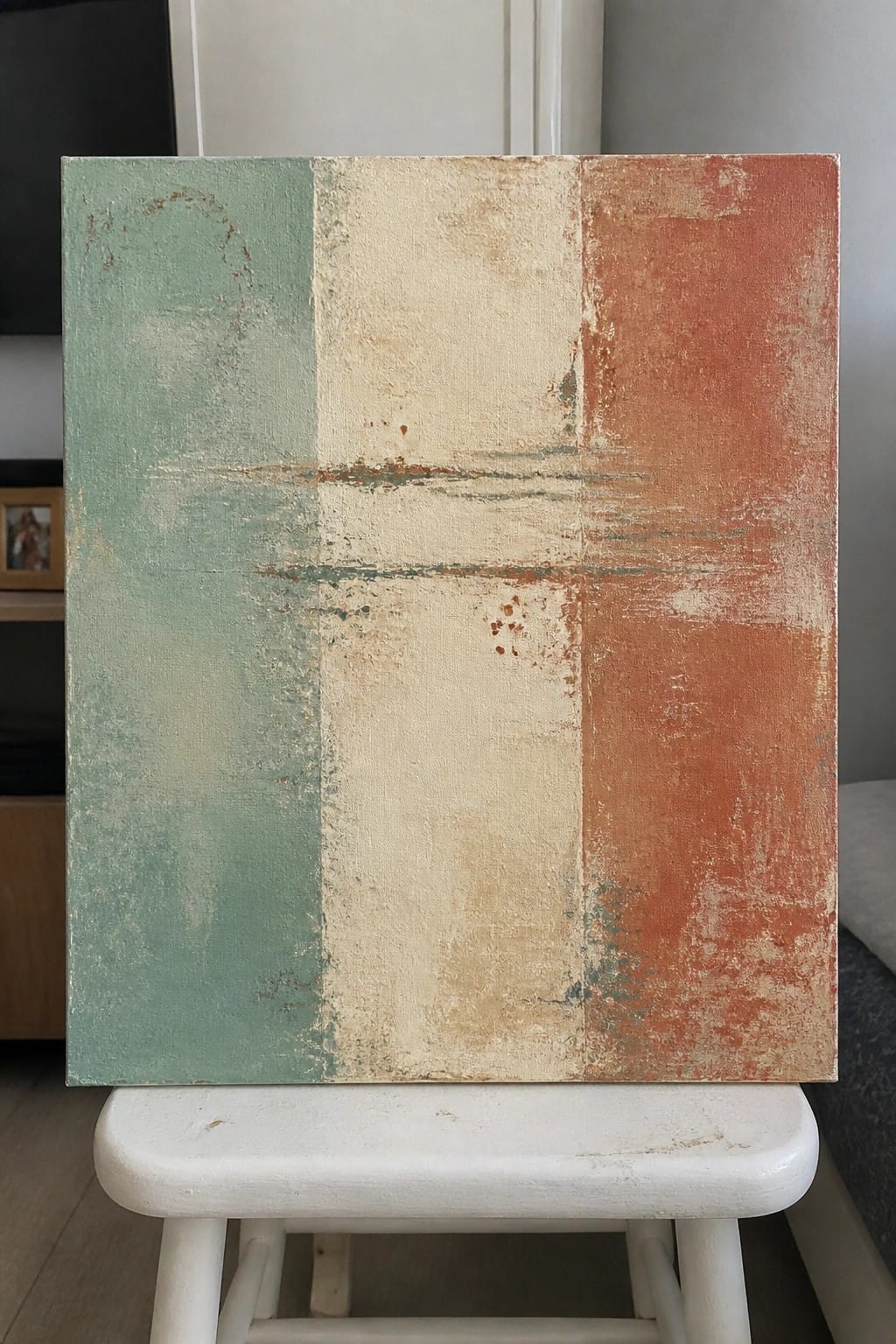 Abstract painting with distressed green, beige, and rust panels on white stool.