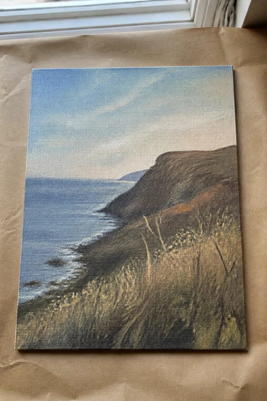 Canvas painting of grassy cliffs overlooking blue ocean under cloudy sky