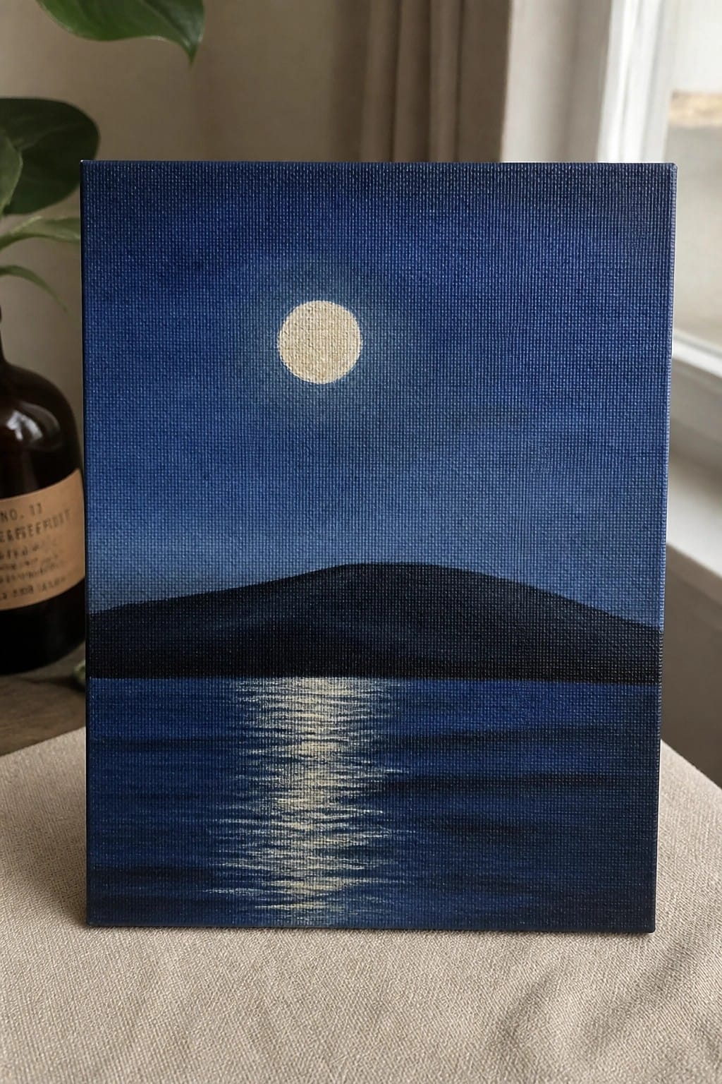 Canvas painting of full moon glowing over dark blue water with distant hill reflection