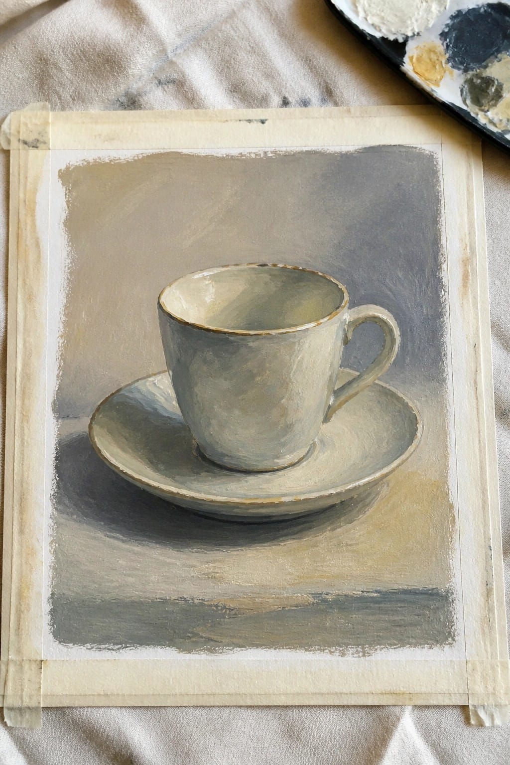 Beige teacup and saucer painting on taped paper beside artist palette