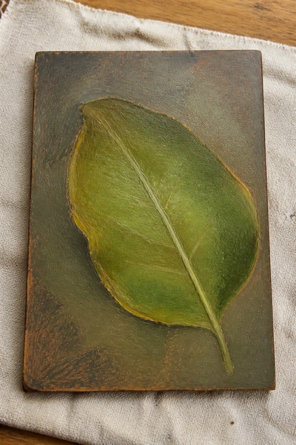 Green leaf painting with veins on dark textured panel atop white fabric