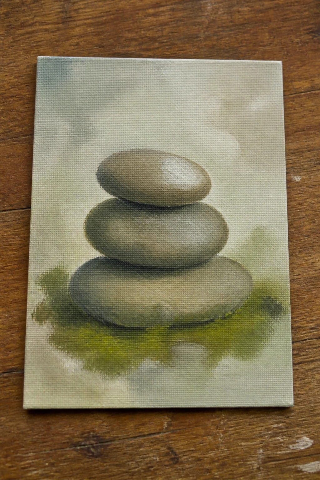 A small oil painting of three stacked gray stones on a canvas with a soft green and gray background.