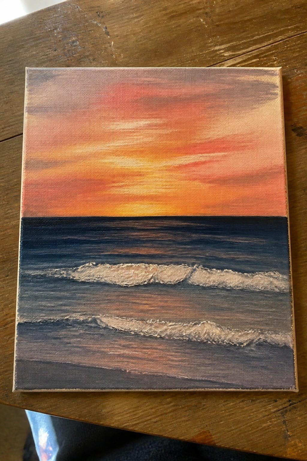 Sunset painting with orange-red sky over dark blue ocean and white waves on wood