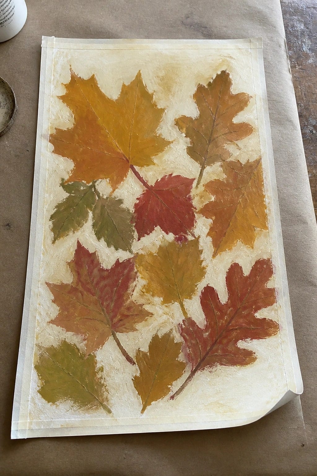 Colorful painted autumn leaves in orange, red, yellow, and green on beige paper.