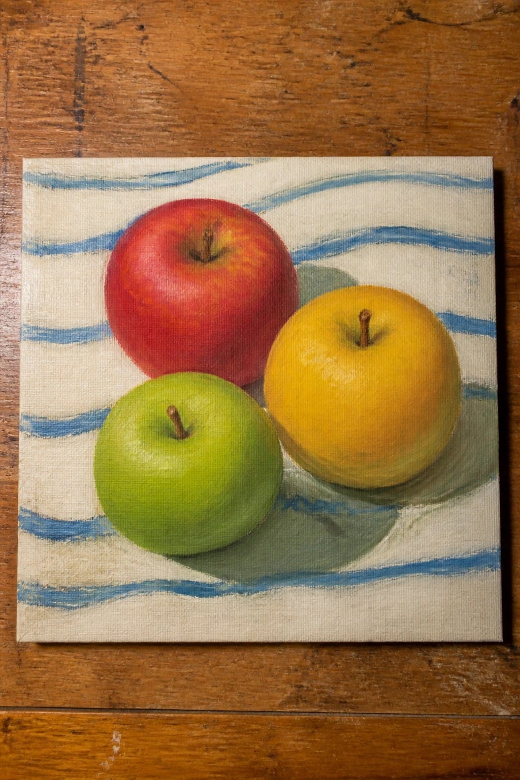 Red, yellow, and green apples on blue-striped white cloth over wooden surface.