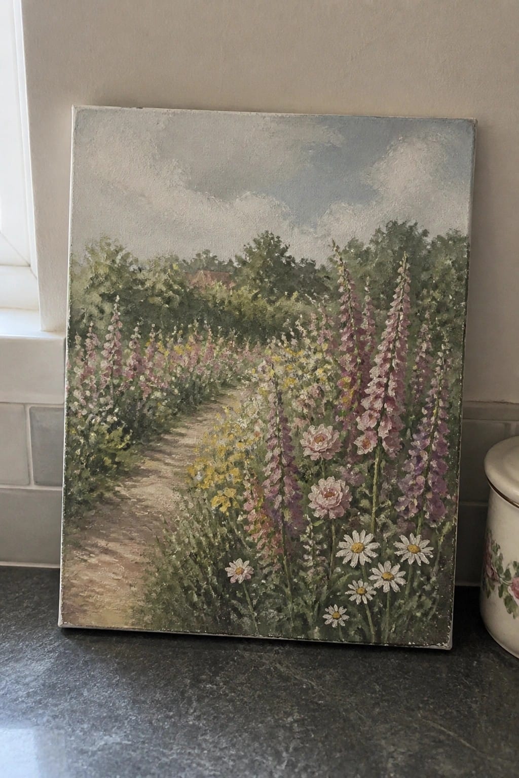 Impressionistic painting of a winding garden path lined with tall pink hollyhocks and daisies