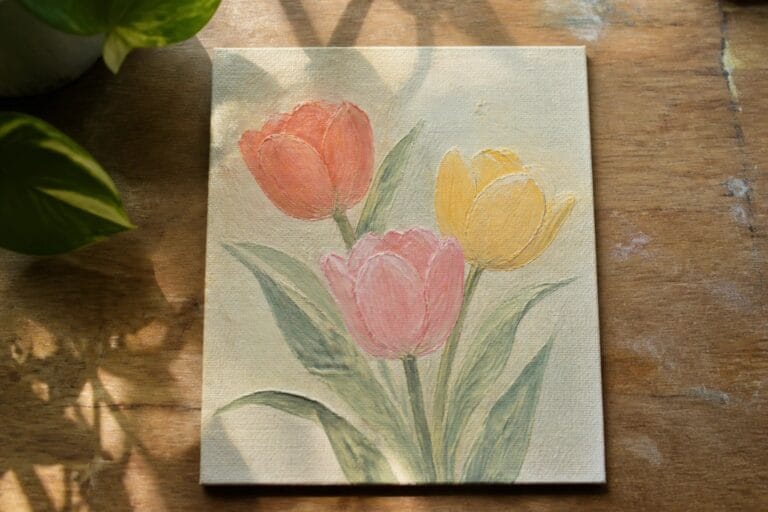 Three tulips painted in coral, yellow, and pink with green leaves on canvas