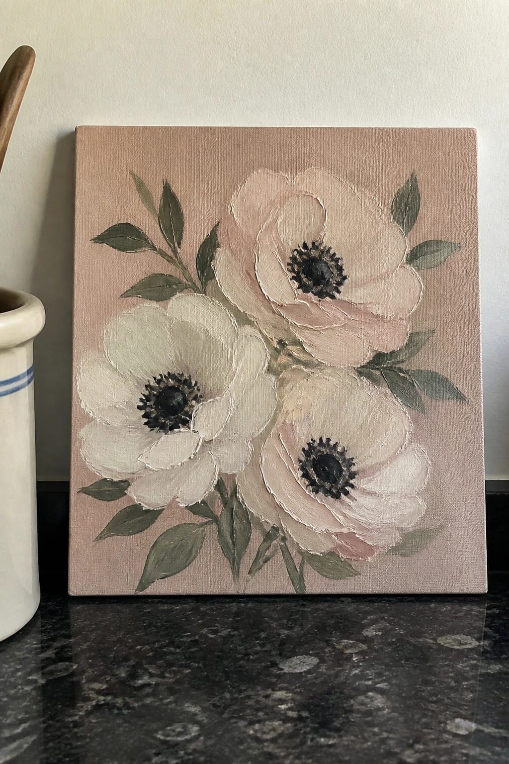 Painting of three white and pink flowers with dark centers and green leaves on pink canvas.