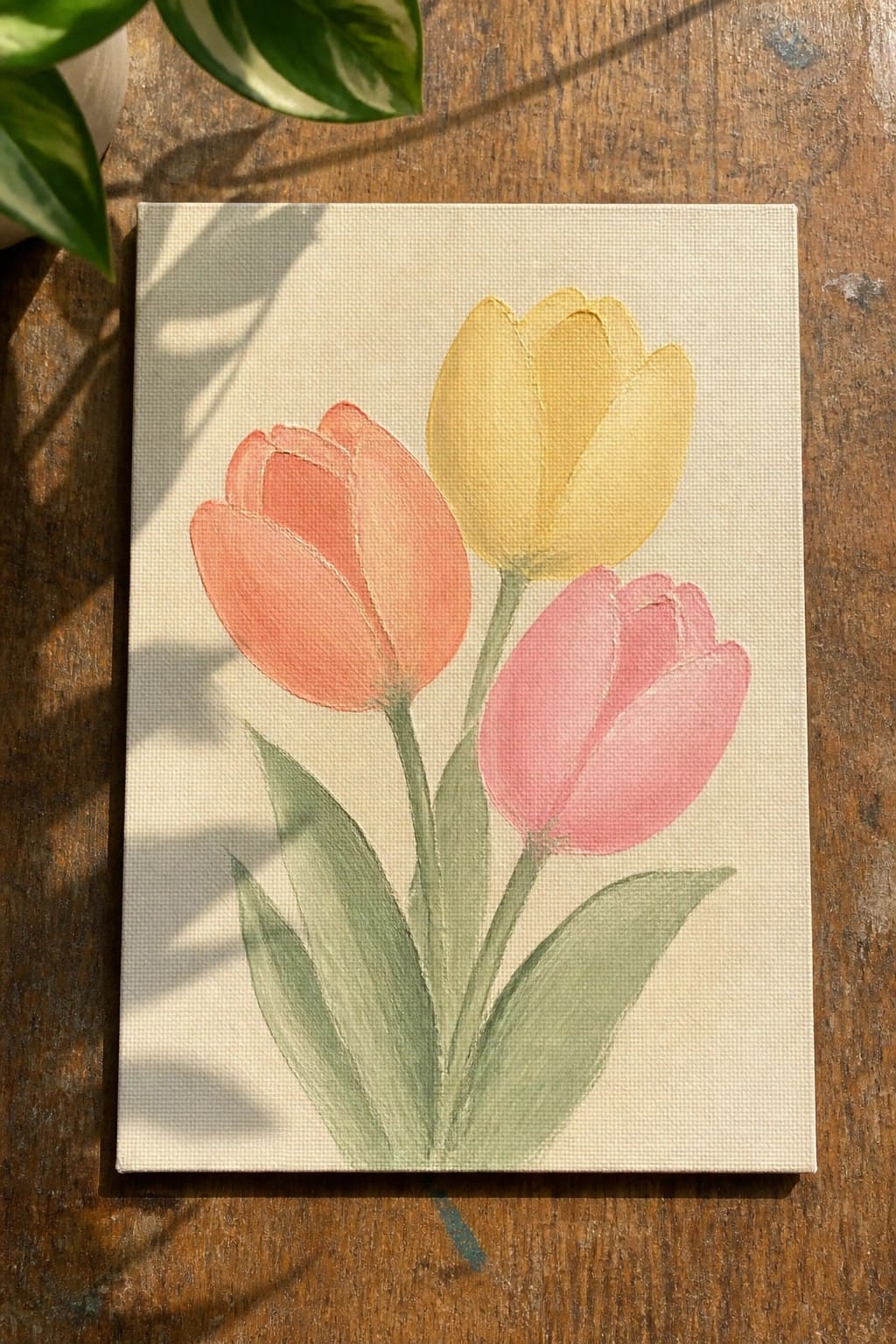 Three tulips painted in coral, yellow, and pink with green leaves on canvas
