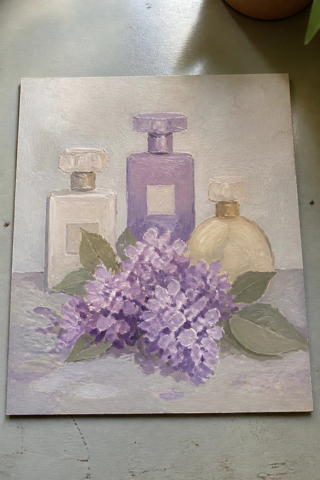 An oil painting of three perfume bottles next to a cluster of purple lilac flowers on a light surface.