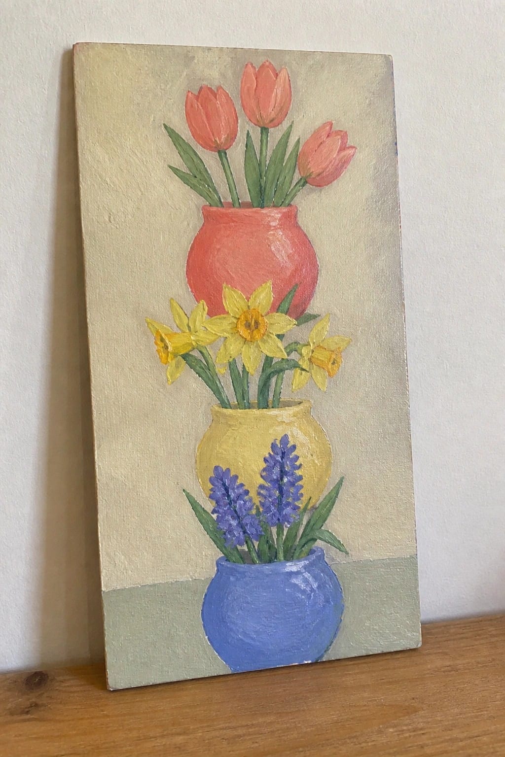 Painting of stacked red, yellow, and blue vases with pink tulips, yellow daffodils, and purple hyacinths.