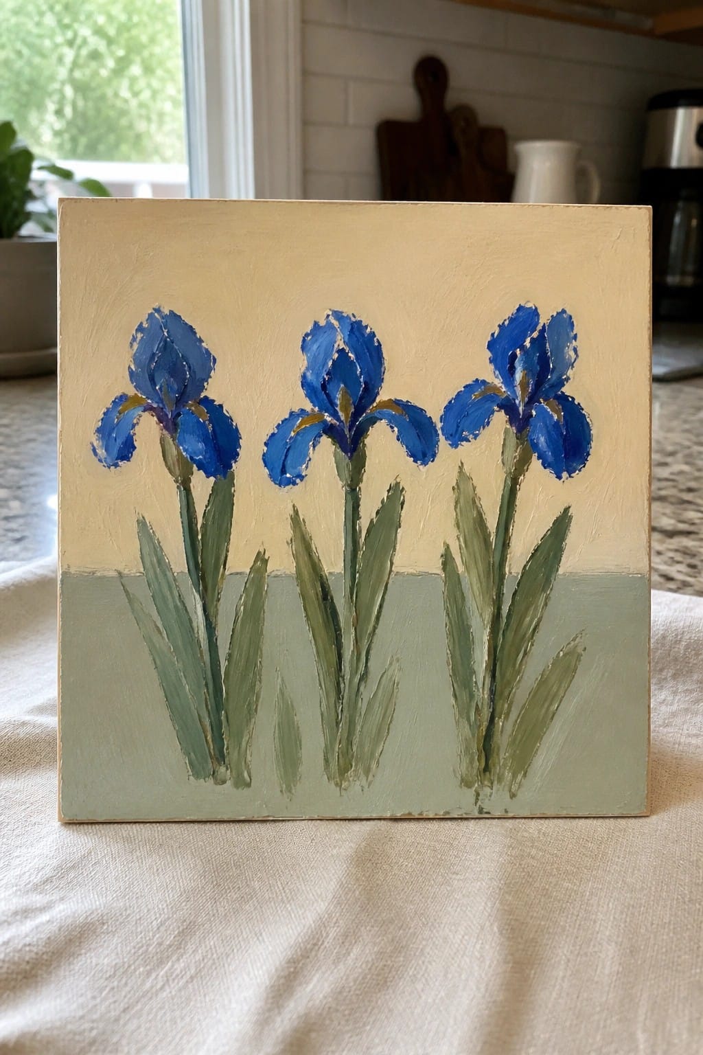 Three blue irises with green stems on beige and green painted canvas