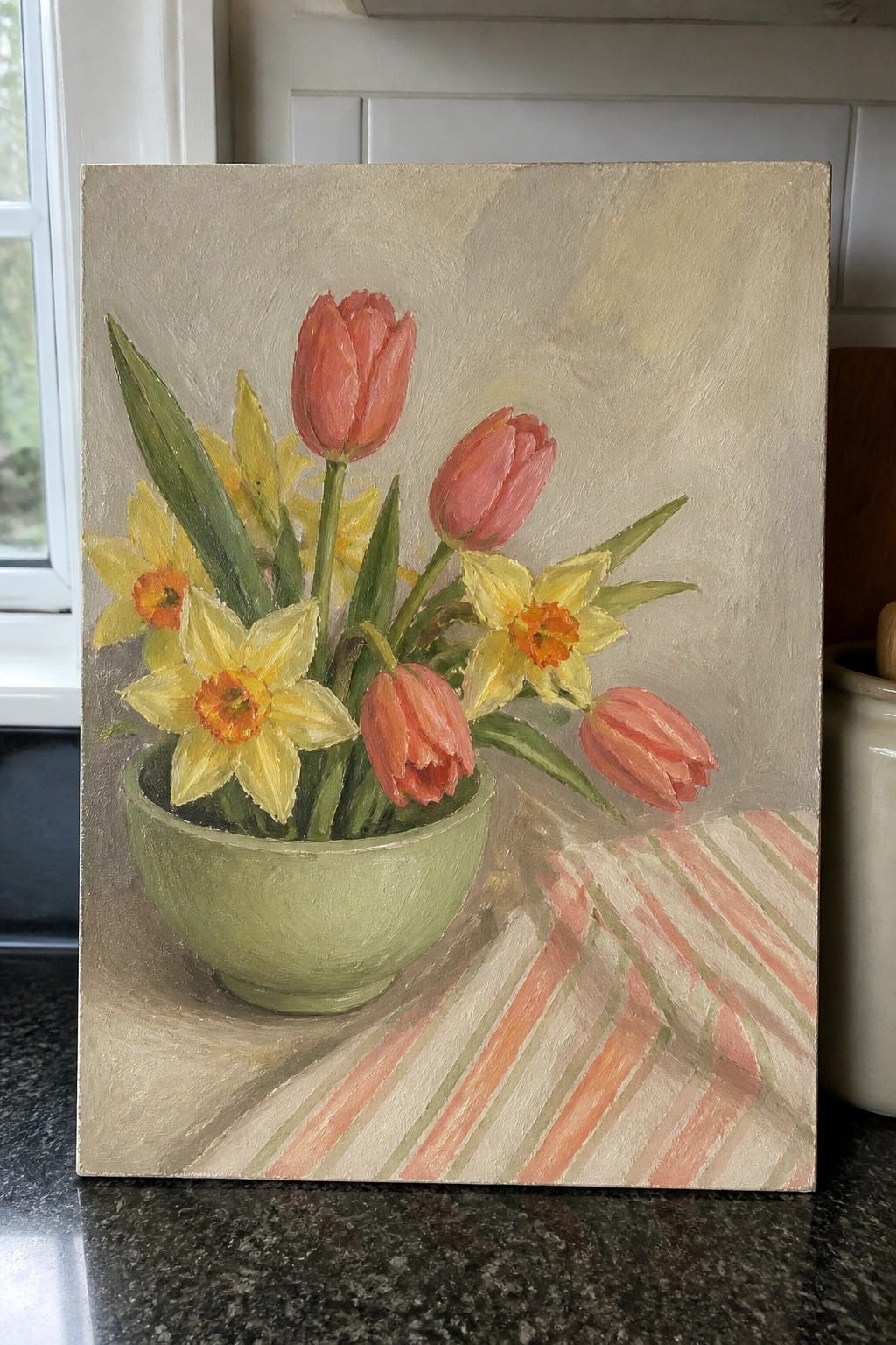 Impressionistic still life of pink tulips and yellow daffodils in a green bowl on striped cloth.