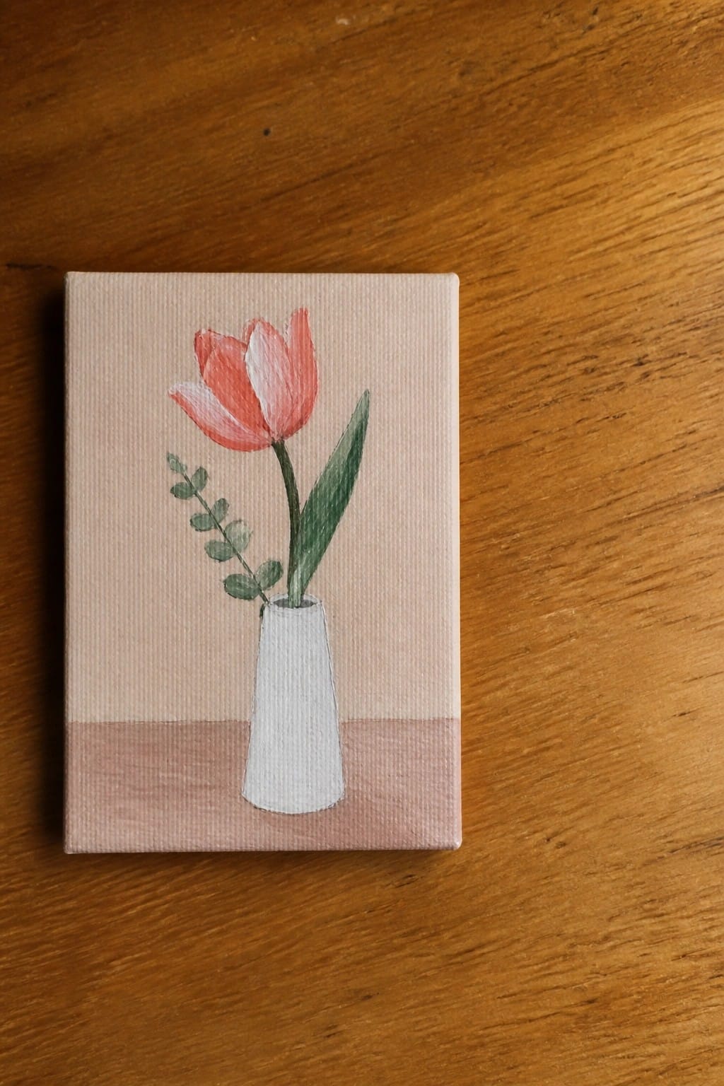 Small canvas painting of coral tulip in white vase on wooden surface
