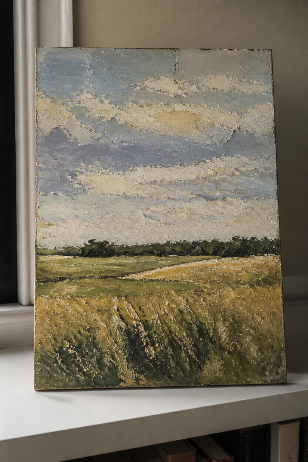 Thickly textured landscape painting of fields and sky on white windowsill with books