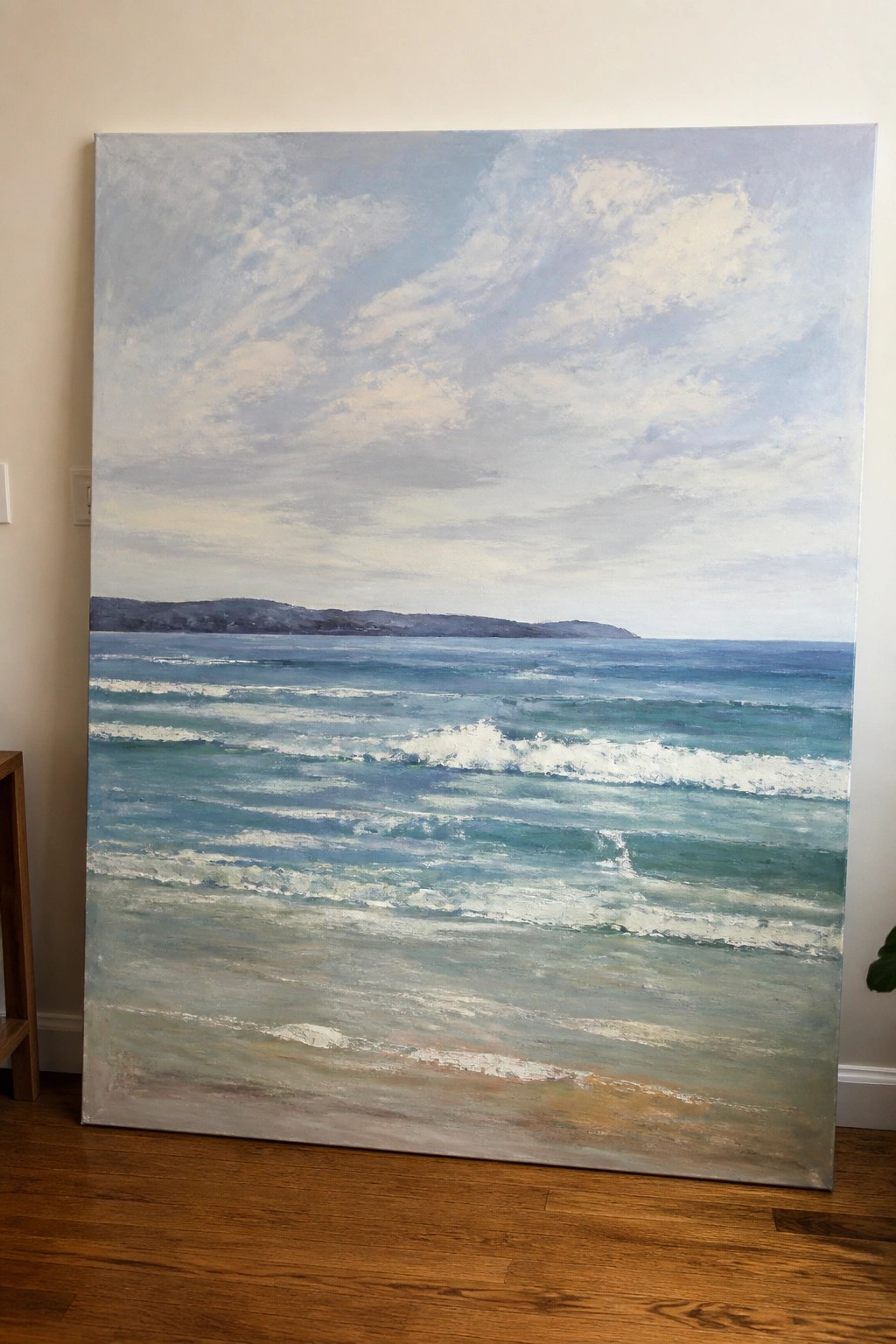 Large seascape canvas with waves and distant hills resting on wooden floor