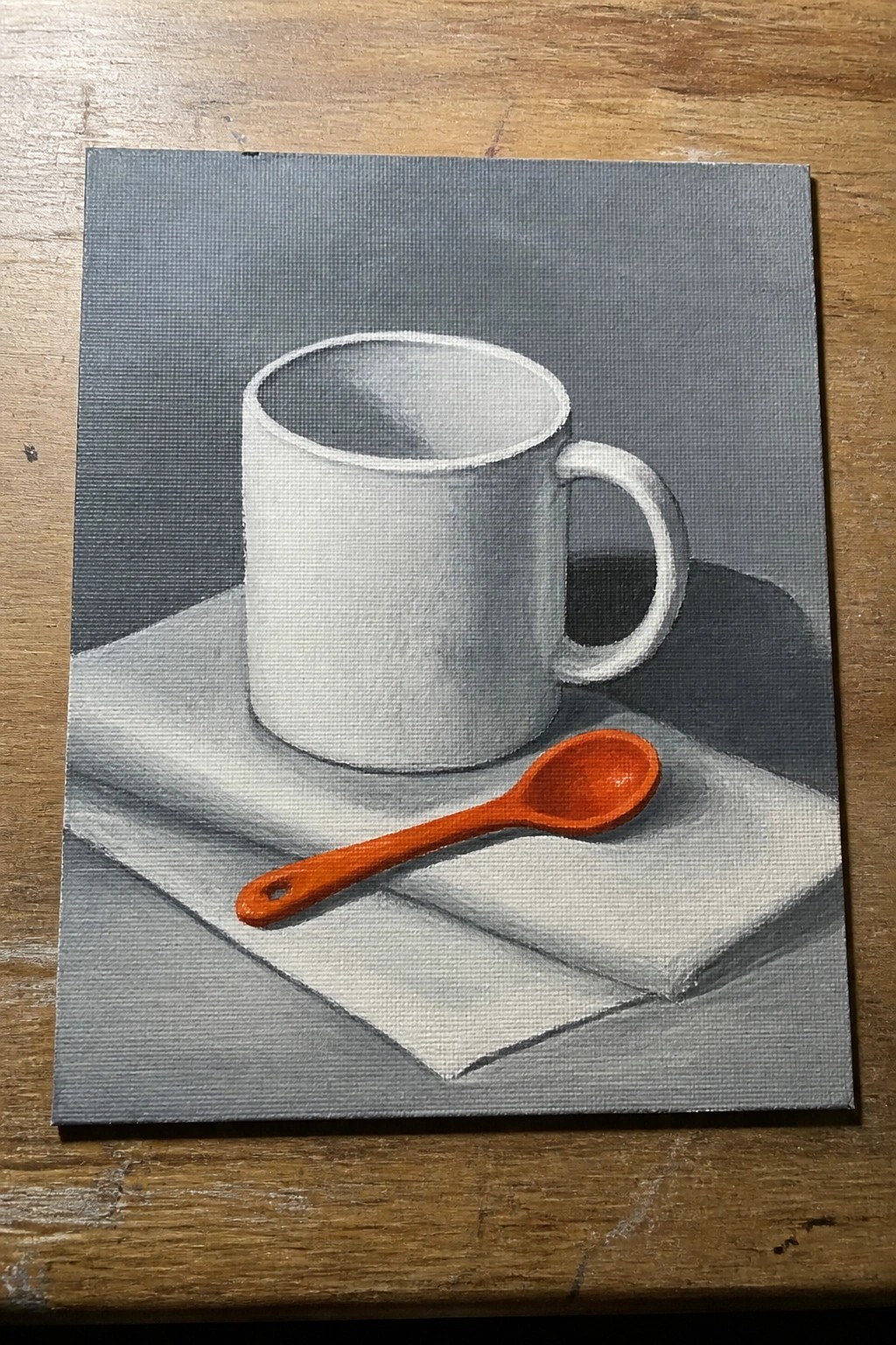 An oil painting of a white mug on a white cloth with an orange spoon placed in front of it on a gray background.