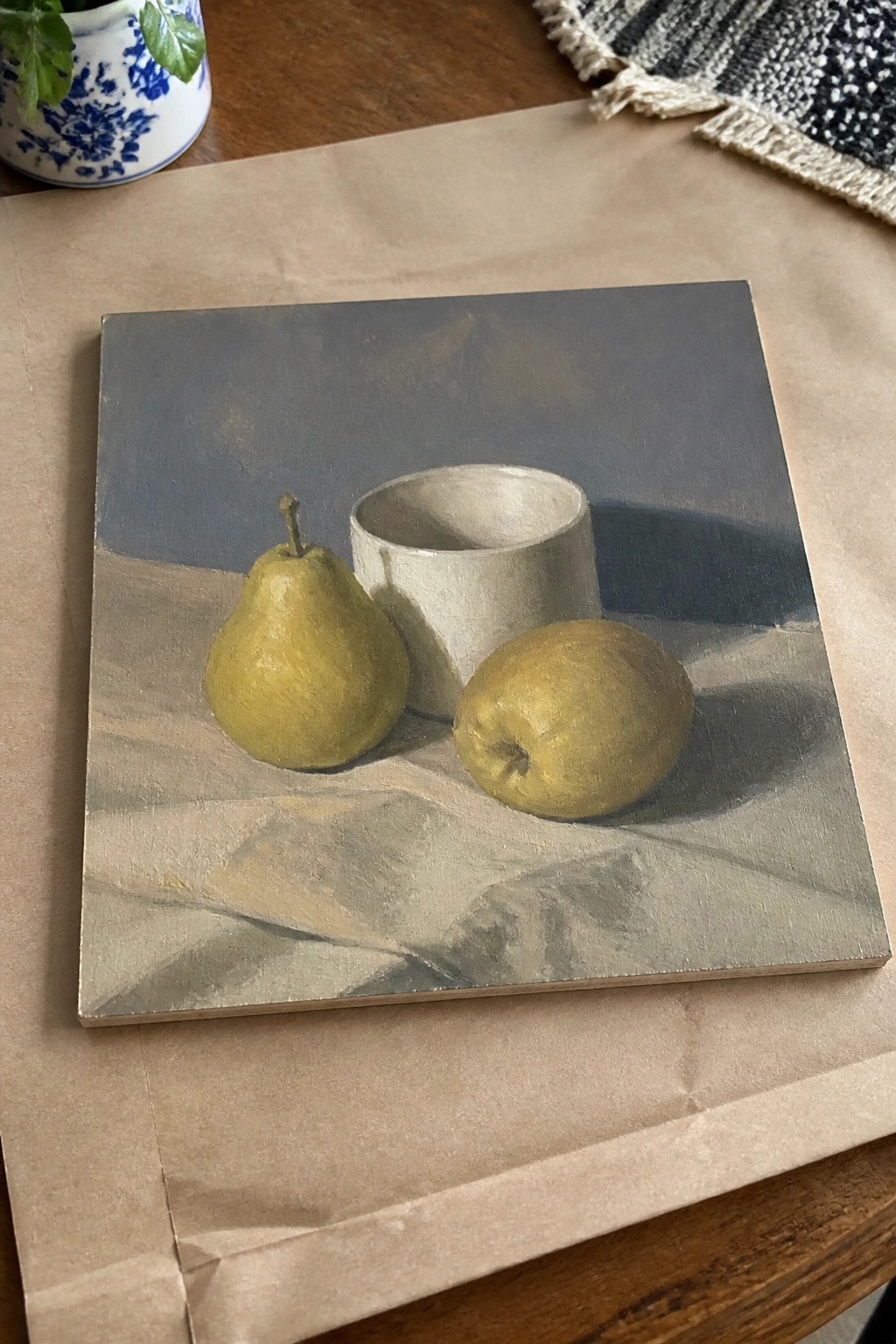 Still life painting of two yellow pears beside a white cylindrical cup on gray cloth