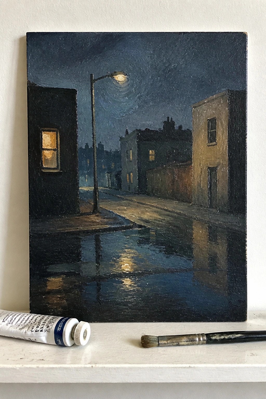 Nocturnal city street painting with wet reflections, paint tube and brush in foreground