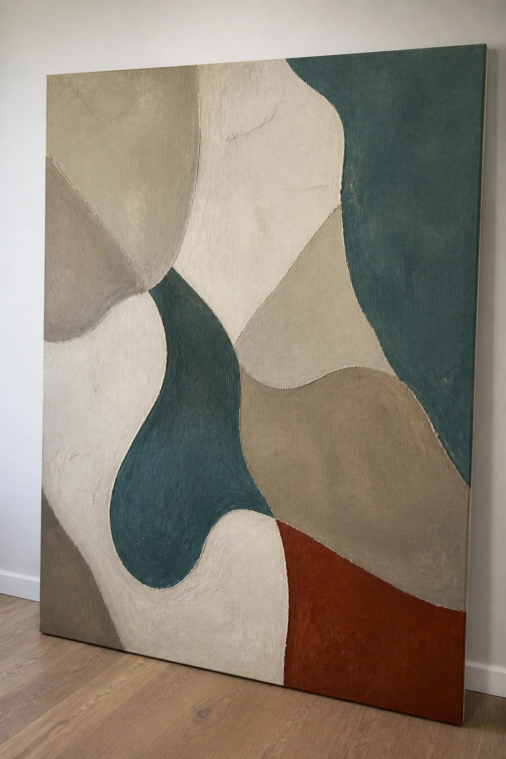 Abstract painting with organic shapes in beige, teal, brown, and rust leaning on wall