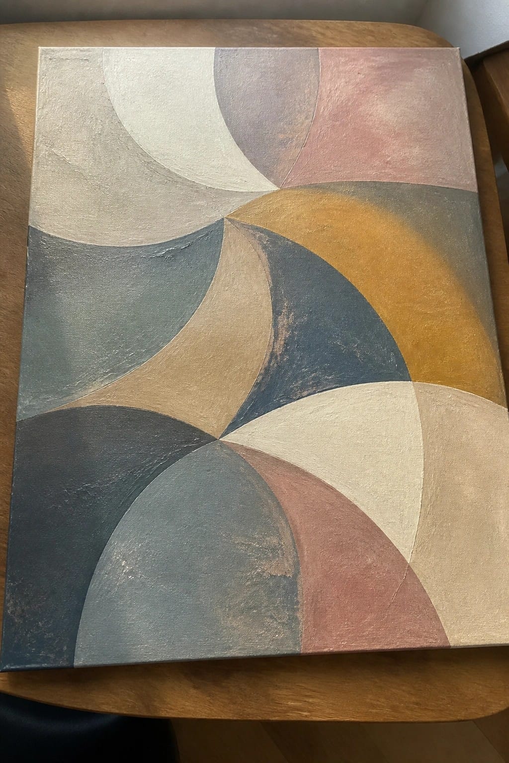 An abstract oil painting with overlapping curved shapes in muted beige, gray, blue, pink, and yellow tones on a rectangular canvas.