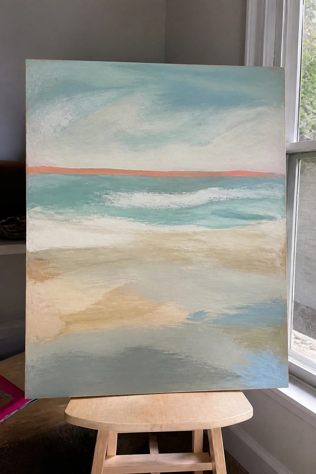 Abstract seascape painting on wooden easel with turquoise sky, ocean waves, and sandy beach